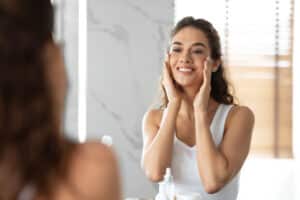 Woman looking in the mirror smiling after a chemical peel in Philadelphia Main Line, PA